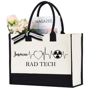 May include: White canvas tote bag with black trim and handles. The bag has a black and white ribbon bow and a black design that says "Jasmine RAD TECH" with a heart and a radiation symbol.