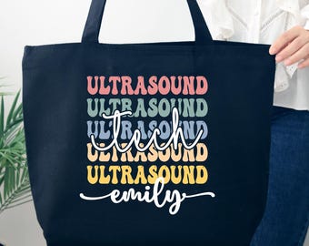 May include: Black canvas tote bag with the text "Ultrasound Tech" in rainbow colors and the name "emily" in white cursive writing.