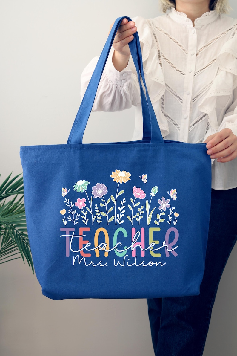 May include: A royal blue canvas tote bag with a colorful floral design and the text "Teacher Mrs. Wilson".