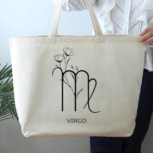 May include: A white canvas tote bag with black floral and zodiac design. The bag features a Virgo zodiac symbol with a floral design and the word "VIRGO" printed below.