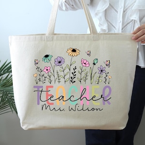 May include: A white canvas tote bag with a colorful floral design and the text "teacher Mrs. Wilson".