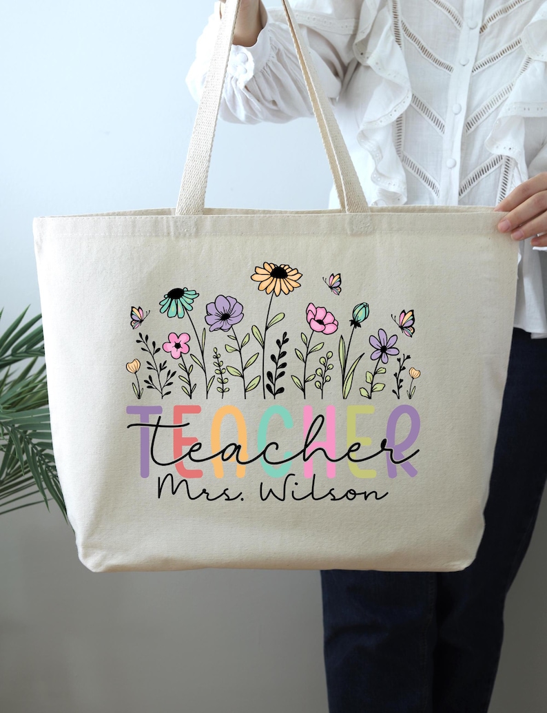 May include: A white canvas tote bag with a colorful floral design and the text "teacher Mrs. Wilson".