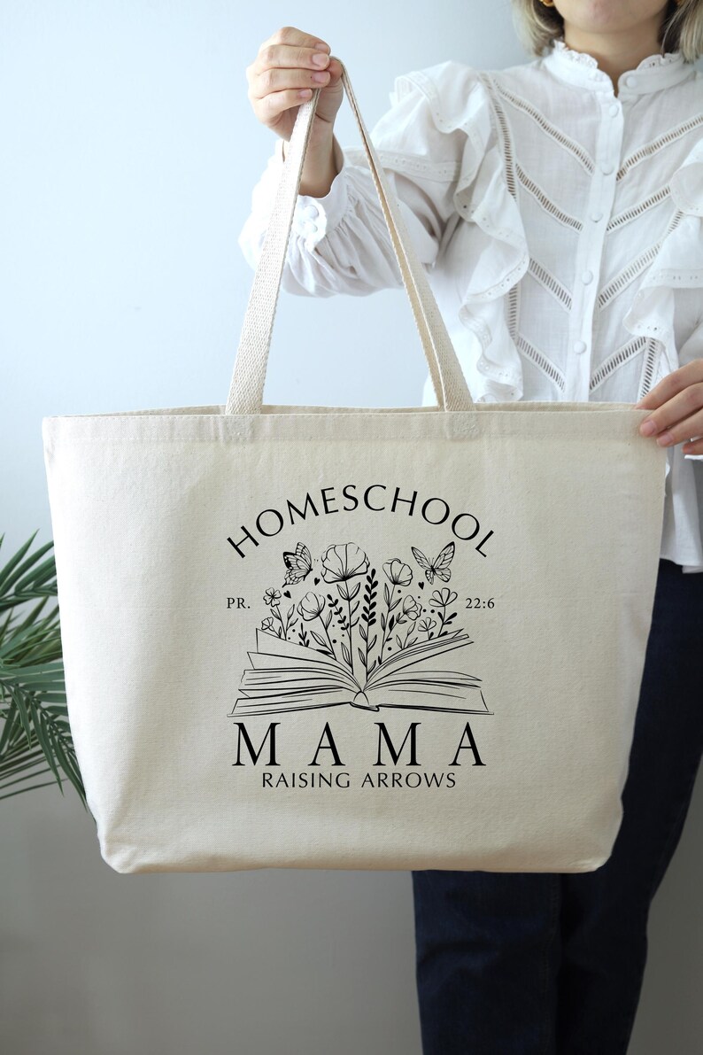 Puede incluir: Una bolsa de lona beige con texto negro y un dise&ntilde;o gr&aacute;fico. El texto dice "Homeschool Mama Raising Arrows" con un libro y un gr&aacute;fico de flores. El libro tiene el texto "PR. 22:6".