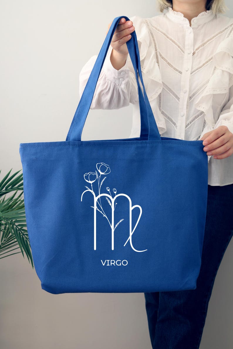 May include: A blue canvas tote bag with a white Virgo zodiac sign and floral design. The text "VIRGO" is printed below the sign.