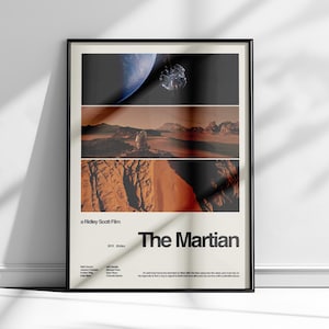 May include: Framed movie poster for "The Martian" film. The poster features a black frame and a design with three horizontal panels showing space and desert landscapes. The title "The Martian" is displayed in bold, black text.