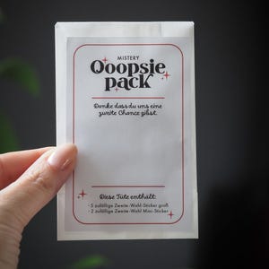 Könnte beinhalten: Ein weißer Papierumschlag mit rotem Rand und dem Text "MISTERY Ooopsie pack" sowie "Danke dass du uns eine zweite Chance gibst." und "Diese Tüte enthält: 5 zufällige Zweite-Wahl-Sticker groß 2 zufällige Zweite-Wahl Mini-Sticker".