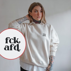 Może przedstawiać: Kremowa bluza z nadrukiem "fck afd." w kolorze czarnym na przodzie.