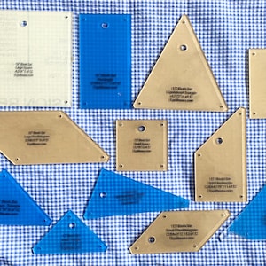 May include: A collection of translucent beige and blue acrylic quilting templates in various geometric shapes including squares, triangles, parallelograms, and rectangles. Each piece features printed text labels, small circular holes, and grid markings.