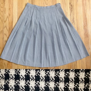 May include: A vintage, knee-length skirt in a classic houndstooth pattern. The skirt features a pleated design in black and white, offering a timeless aesthetic. The fabric appears to be a woven material, suitable for various occasions.