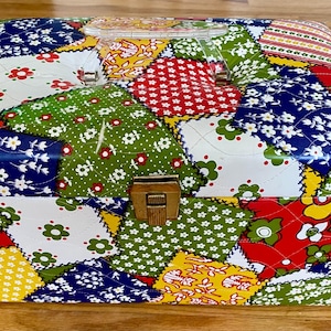 May include: A vintage hexagonal box with a patchwork design. The box features a variety of colorful floral patterns in red, green, blue, and yellow. It has a wooden clasp and a clear plastic handle.