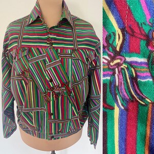 May include: A colorful, vintage jacket with a vibrant striped pattern in green, red, purple, and yellow. The jacket features a collared neckline, button-up front, and decorative tassels. The design includes vertical and horizontal stripes, creating a unique patchwork effect.