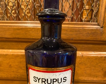 May include: A cobalt blue glass bottle with a gold and red label that reads "SYRUPUS".