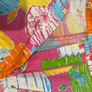 May include: Close-up of a colorful fabric with a vibrant floral and geometric pattern. The design features pink, yellow, orange, and blue hues with a zipper detail. The fabric is likely used for clothing or accessories.