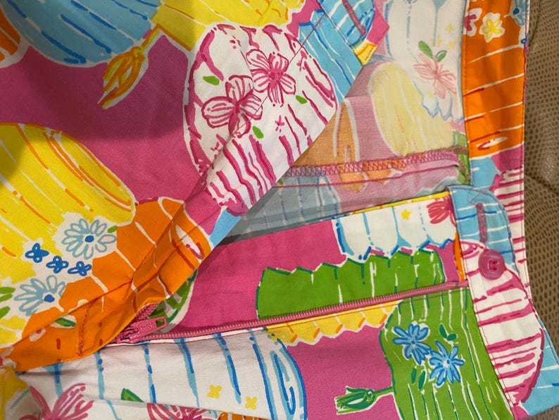 May include: Close-up of a colorful fabric with a vibrant floral and geometric pattern. The design features pink, yellow, orange, and blue hues with a zipper detail. The fabric is likely used for clothing or accessories.