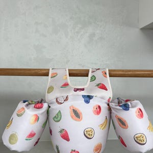 May include: White and light pink swim float with a fruit pattern. The float has two arm floaties with a white and light pink fruit pattern. The arm floaties are attached to the main float with a white strap.