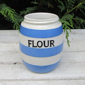 May include: A white and blue striped ceramic flour canister with the word "FLOUR" printed in black.