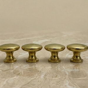 Peut inclure: Quatre boutons de meuble en laiton avec un dessus arrondi et une base cylindrique. Les boutons sont disposés en rangée et ont une surface polie et réfléchissante. Ces boutons décoratifs conviennent aux projets de meubles et de décoration intérieure.