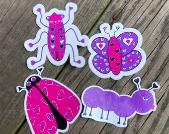 May include: Four colorful stickers featuring a purple and pink butterfly, a purple and pink caterpillar, a pink ladybug, and a purple and pink bug. Each sticker has a heart pattern.