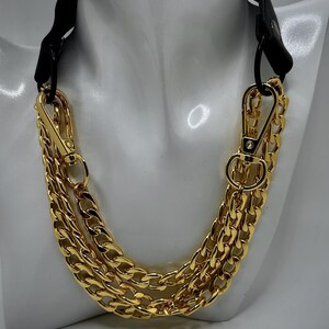May include: A gold chain necklace with a black leather strap. The chain is made of three thick, linked chains.