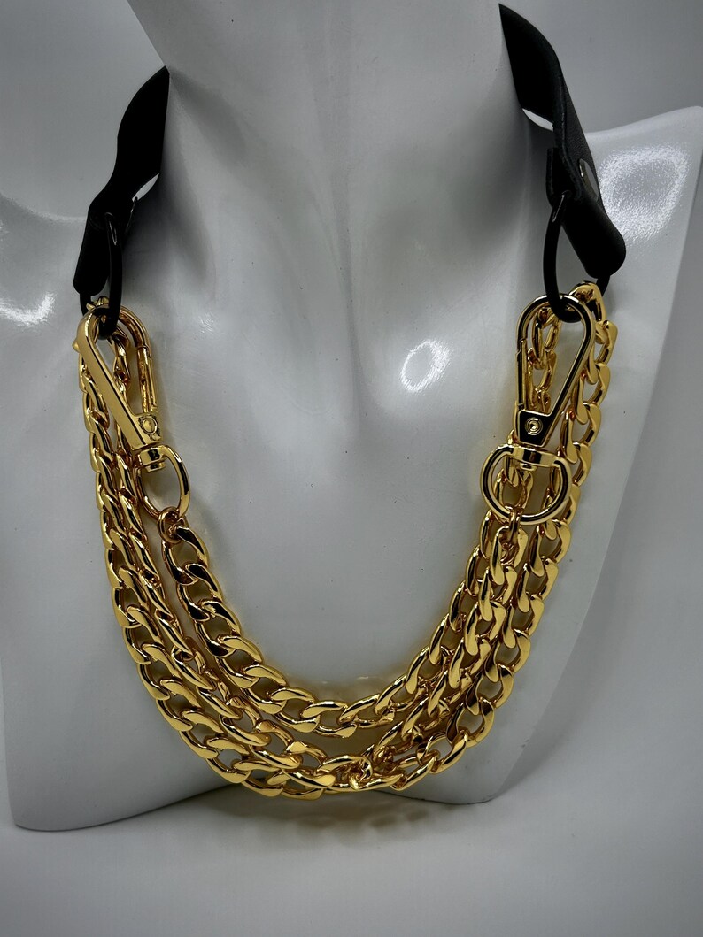 May include: A gold chain necklace with a black leather strap. The chain is made of three thick, linked chains.