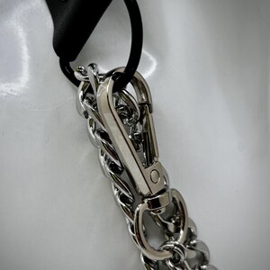 May include: A silver chain with a silver clasp attached to a black leather strap. The chain is a double chain with a twisted design.