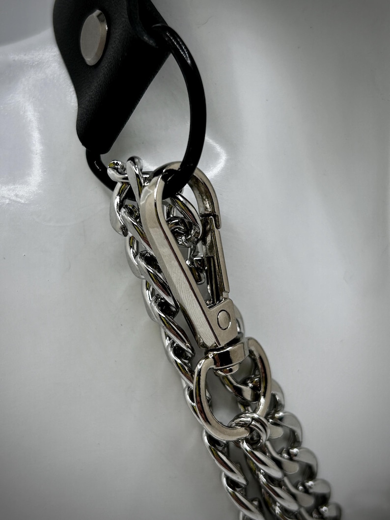 May include: A silver chain with a silver clasp attached to a black leather strap. The chain is a double chain with a twisted design.