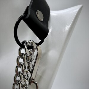 May include: A black leather choker with a silver chain and a silver clasp. The choker is on a white mannequin.