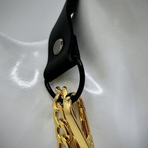 May include: A gold chain necklace with a black leather strap and a gold clasp. The chain is thick and chunky, and the clasp is a simple hook.