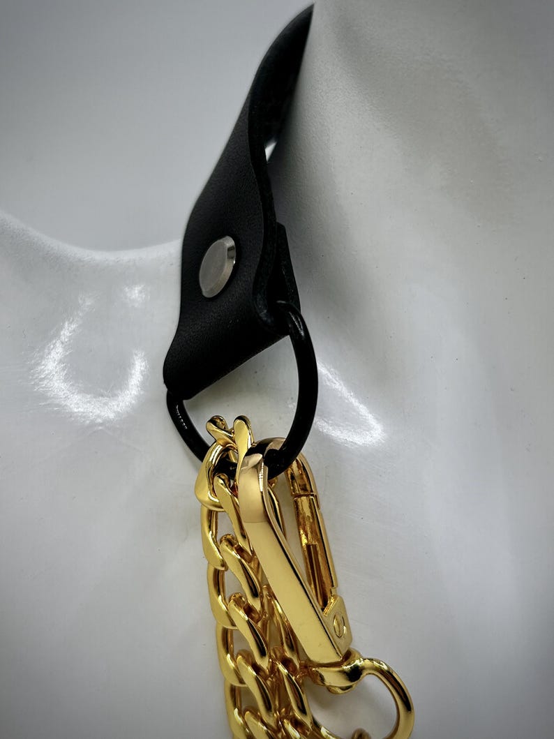May include: A gold chain necklace with a black leather strap and a gold clasp. The chain is thick and chunky, and the clasp is a simple hook.