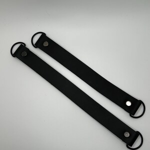 May include: Two black leather handles with metal rings and silver rivets. The handles are approximately 12 inches long.
