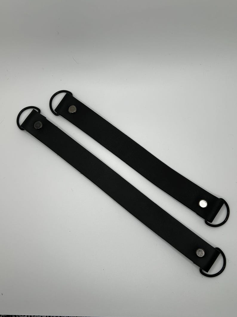 May include: Two black leather handles with metal rings and silver rivets. The handles are approximately 12 inches long.