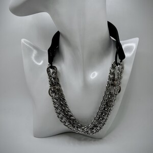 May include: A silver chain necklace with a black leather choker. The chain is made of two thick, linked chains.