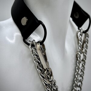 May include: A black leather choker with a silver chain and a silver clasp. The choker has a silver rivet on the leather.
