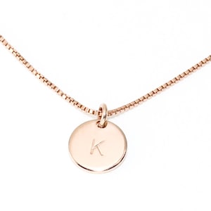 May include: A rose gold necklace with a small round pendant featuring the letter K.