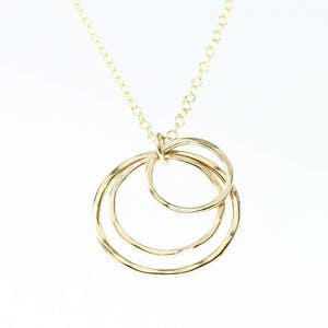 May include: A gold necklace with a pendant featuring three interlocking circles.