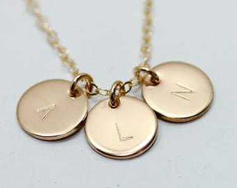 May include: Gold necklace with three round charms, each with a different letter engraved on it. The letters are A, L, and N.