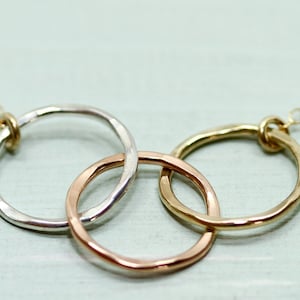 May include: A silver, gold, and rose gold necklace with three interlocking circles. The circles are hammered and have a textured finish.