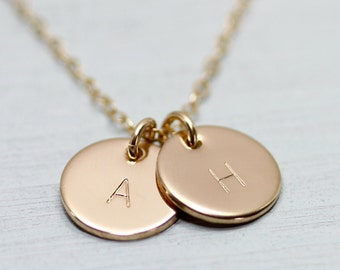 May include: Gold necklace with two round pendants, one with the letter 'A' and the other with the letter 'H'.