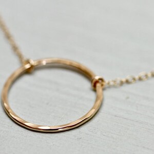 May include: A gold circle pendant necklace with a delicate chain. The circle is hammered and has a textured finish.
