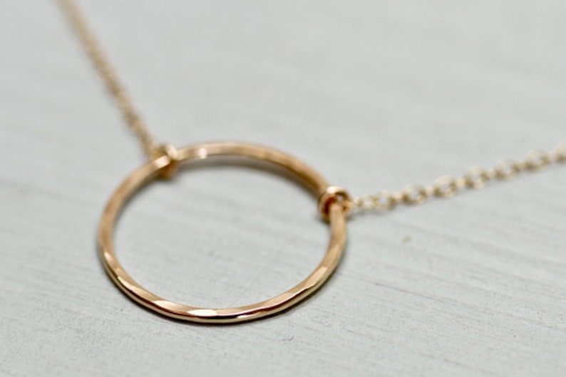 May include: A gold circle pendant necklace with a delicate chain. The circle is hammered and has a textured finish.