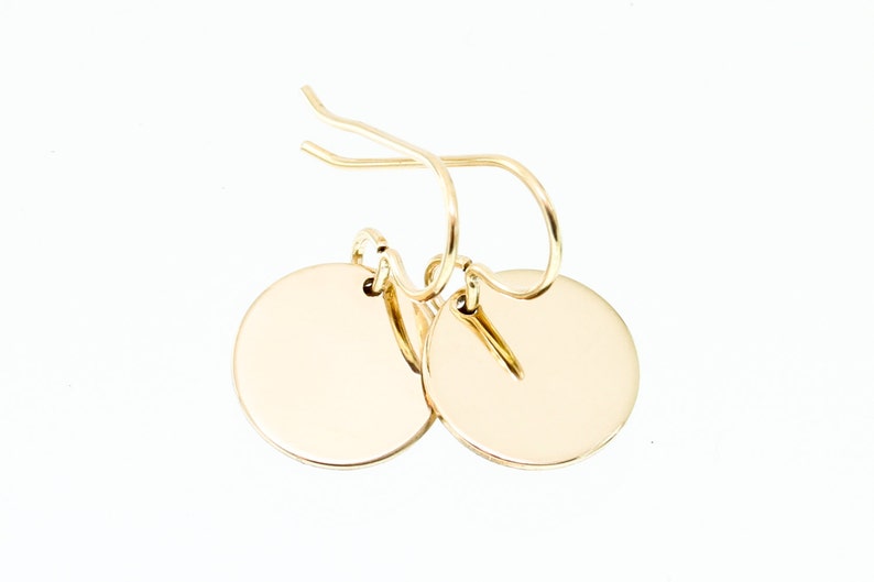 May include: A pair of gold-toned disc earrings with a simple, minimalist design. The earrings have a circular shape and a smooth, polished finish.