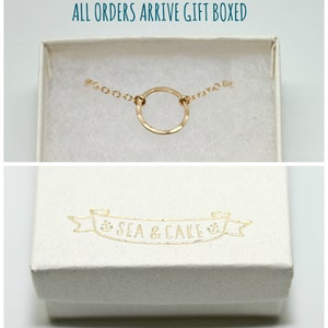 May include: A gold circle necklace with a delicate chain, presented in a white gift box with the text "Sea & Cake" printed on the lid.