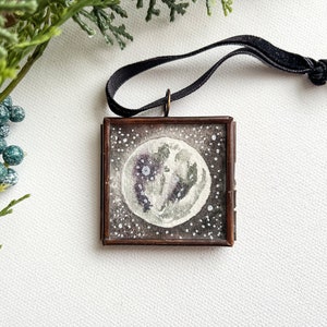 Framed mini watercolor moon ornament in with black velvet ribbon hanger on a white background