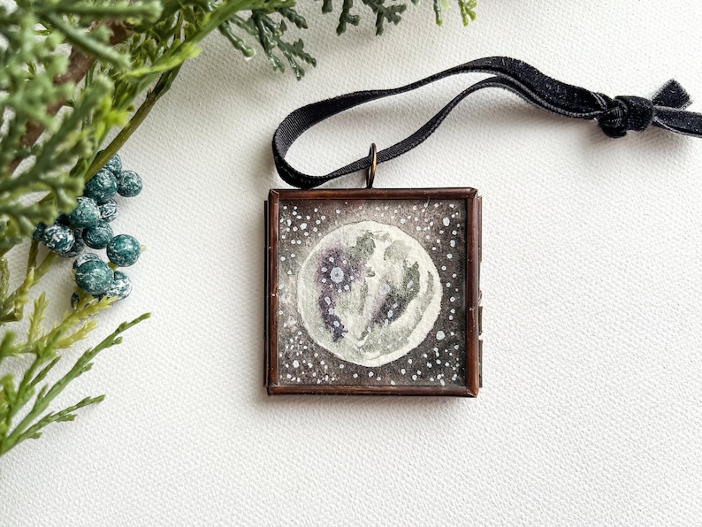 Framed mini watercolor moon ornament in with black velvet ribbon hanger on a white background