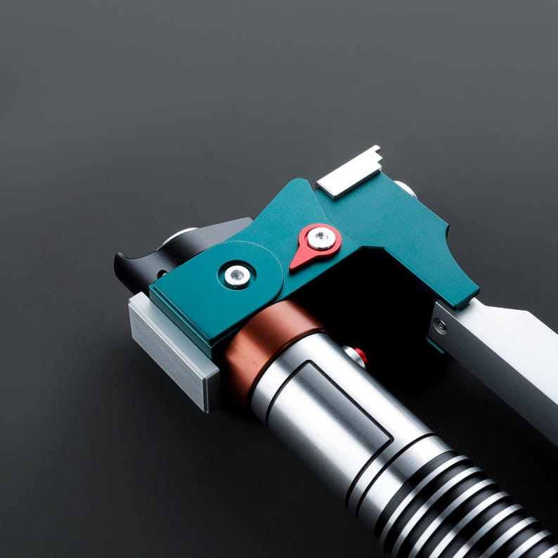 May include: A close-up of a teal and silver lightsaber with a red button. The lightsaber has a black handle and a silver blade.