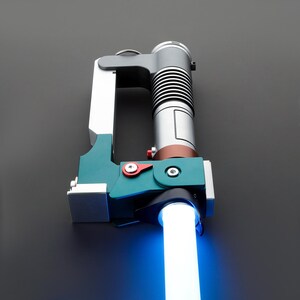 May include: A blue lightsaber with a green and silver hilt. The hilt has a red button and a silver ring.