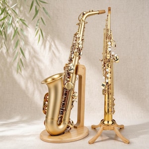 Peut inclure: Un saxophone alto doré posé sur un support en bois à côté d'un saxophone soprano droit sur un trépied en bois. Les deux instruments présentent des clés, des tiges et des pavillons métalliques, avec une finition polie et des détails mécaniques.