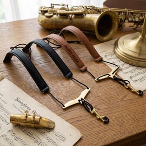 Peut inclure: Deux sangles de saxophone avec des bandes en cuir rembourrées, une noire et une marron clair. La sangle marron clair porte l'inscription custom made. Les deux sangles incluent des cordons noirs, des écarteurs en métal doré et des mousquetons.