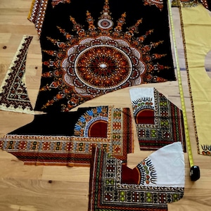 May include: Various pieces of patterned fabric in black, red, orange, and white, possibly for clothing. The fabric features intricate geometric and floral designs. A yellow measuring tape is visible.