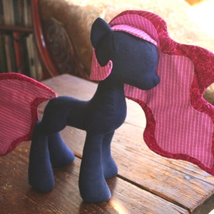 Op de afbeelding: Een pluche speelgoedpaard met een donkerblauw lichaam en een roze-wit gestreepte manen en staart. Het paard heeft een roze-wit gestreepte manen en staart.